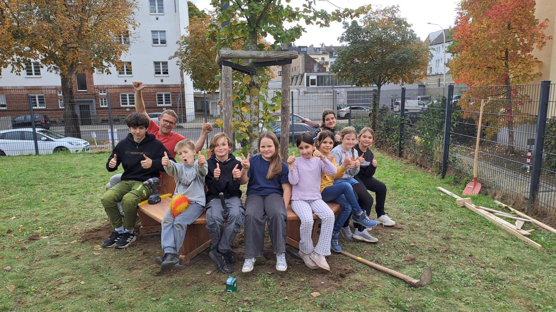 Kinder sitzen auf einer Rundbank um einen Baum