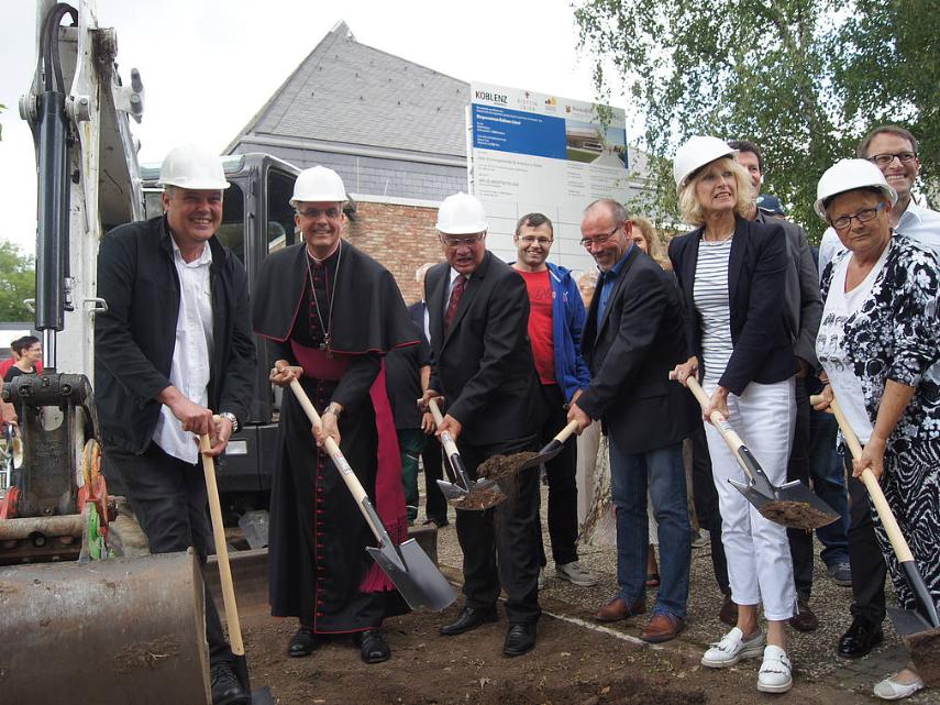 Menschen mit einem Spaten in der Hand stehen zusammen und eröffnen die Baustelle am Bürgerzentrum