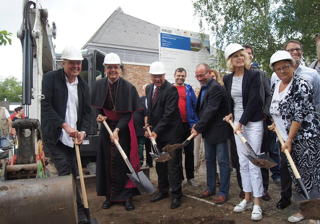 Menschen mit einem Spaten in der Hand stehen zusammen und eröffnen die Baustelle am Bürgerzentrum