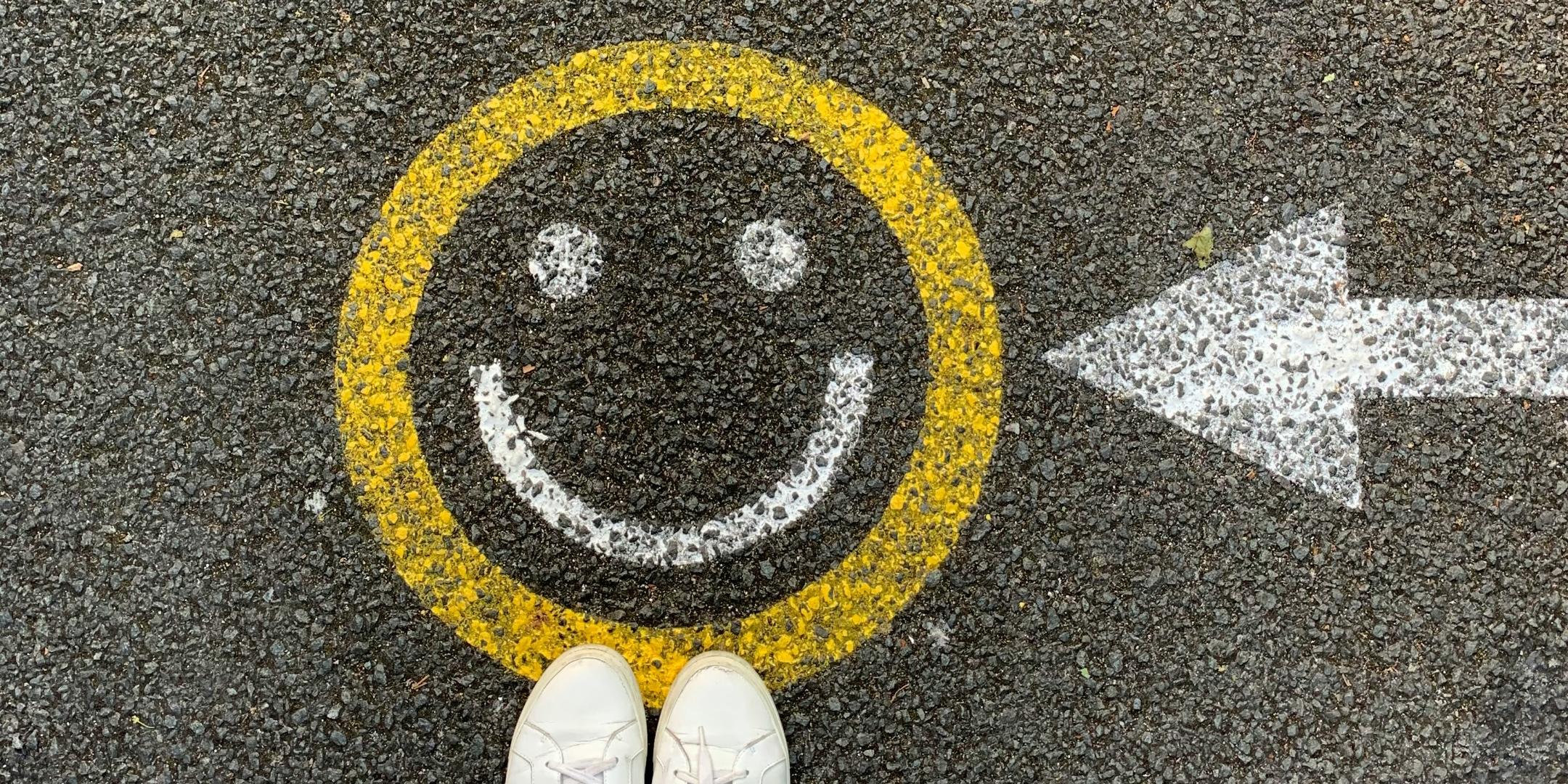 Zwei Füße stehen einem Smiley, das mit Kreide auf die Straße gemalt wurde.