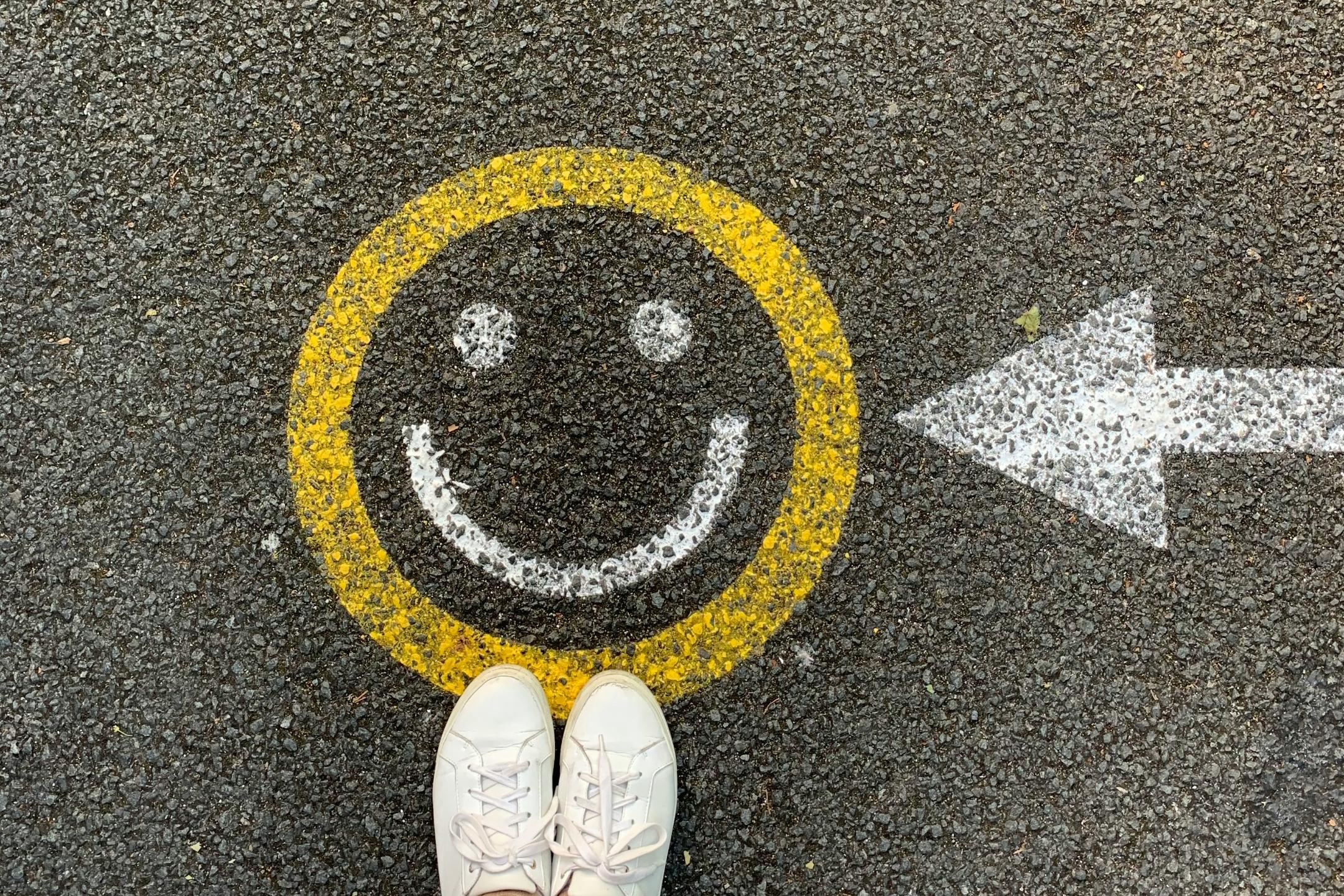 Zwei Füße stehen einem Smiley, das mit Kreide auf die Straße gemalt wurde.